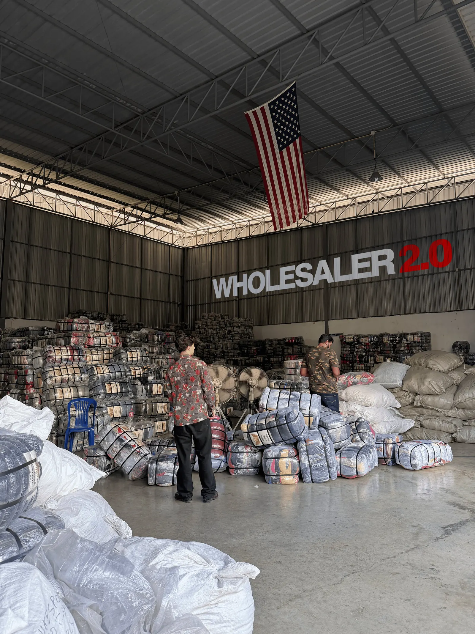 Entrepôt Wholesaler 2.0 rempli de balles de vêtements vintage, avec l'enseigne de la marque au mur