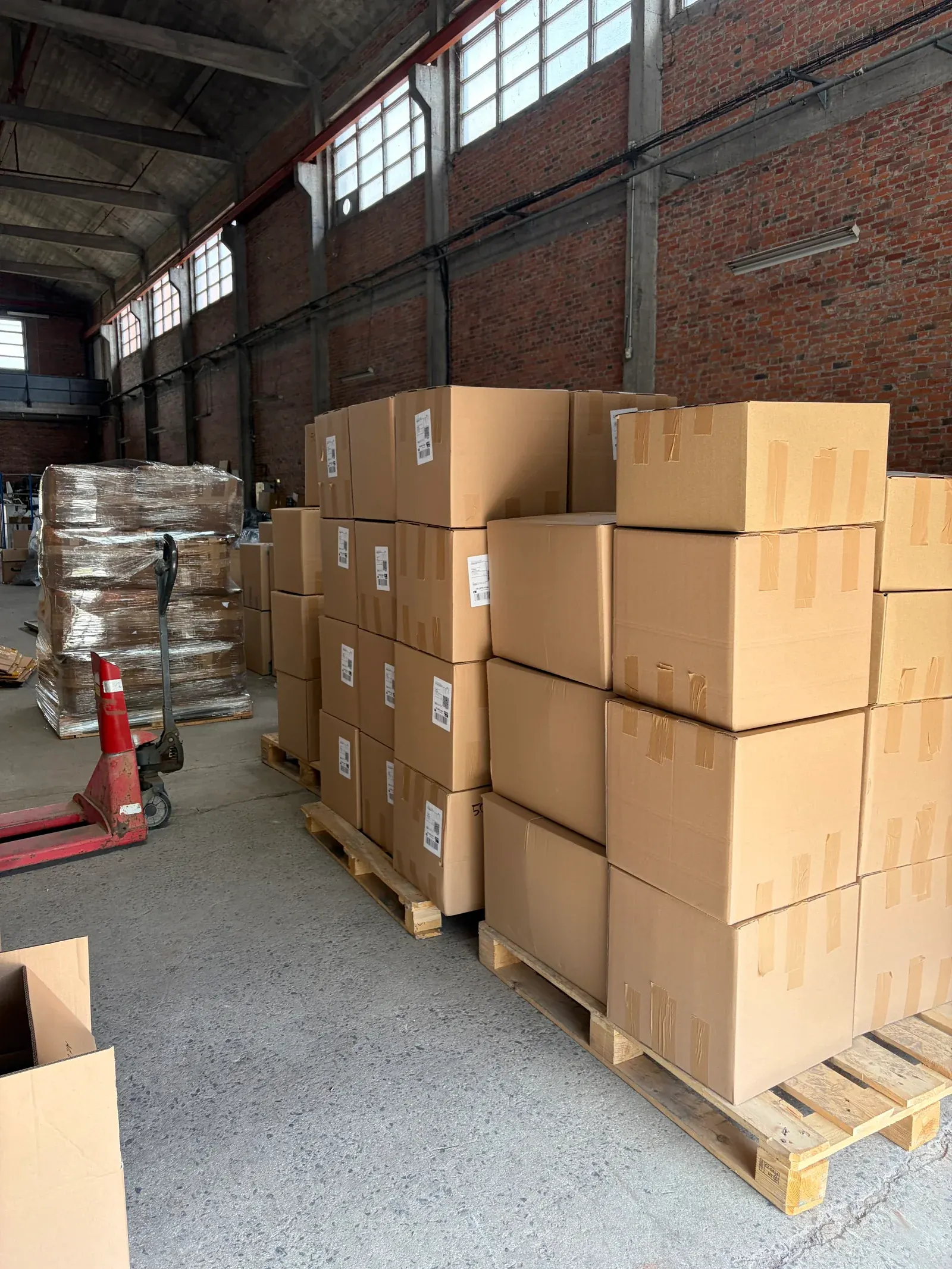 Palettes de cartons de commandes étiquetés, prêts à l'expédition, avec un transpalette dans l'entrepôt